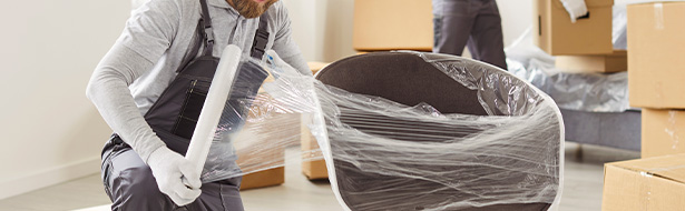 moving company workers wrapping furniture for relocation in a new home with boxes nearby