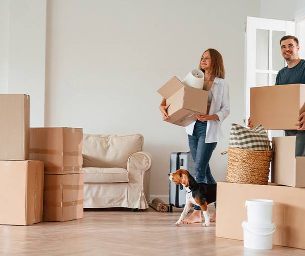 couple moving into new home carrying boxes with dog nearby